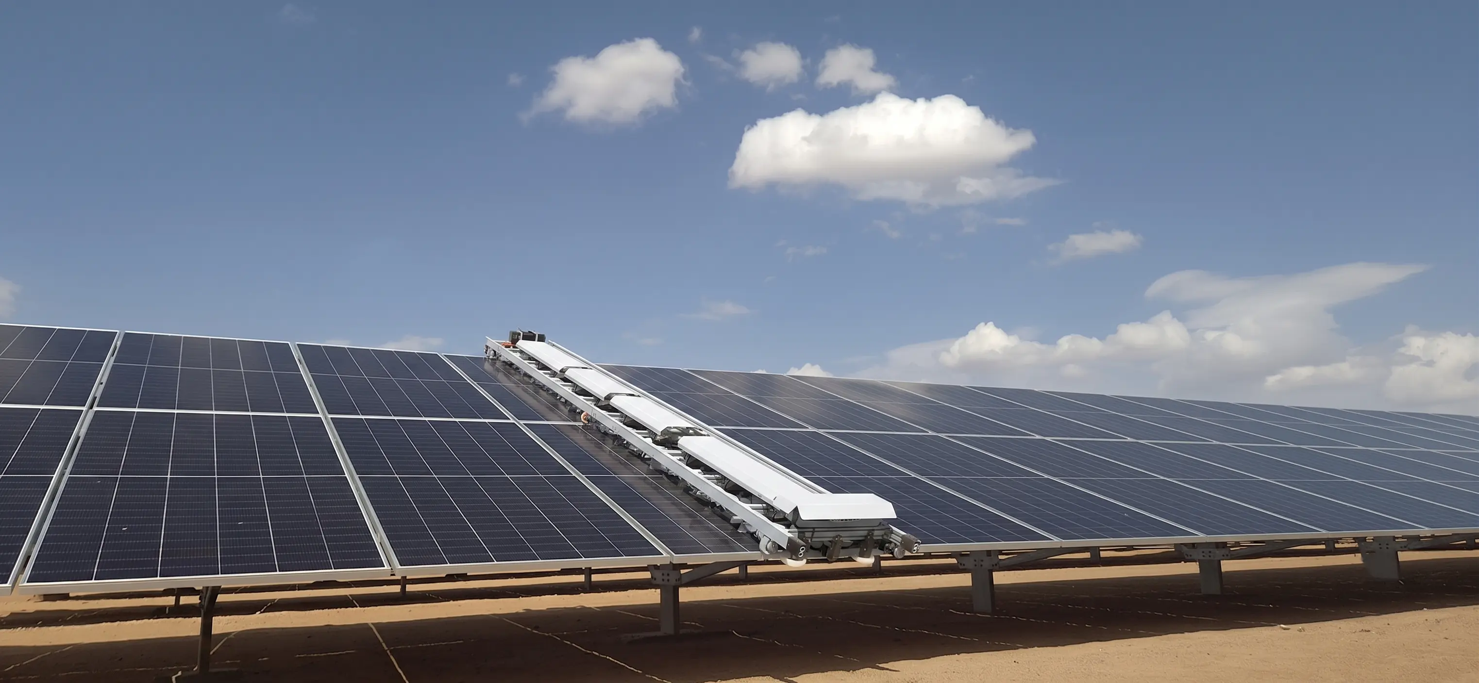 Droid robot operating on a desert solar farm with visible dust terrain and panel rows in early-morning light